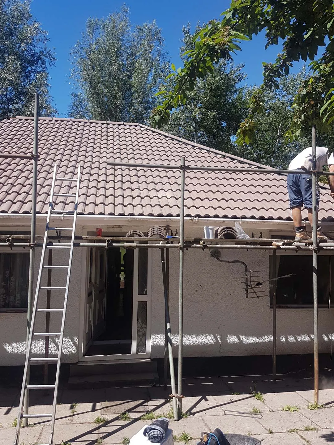 Roofer on scaffold fitting ridge tiles on a hipped bungalow roof