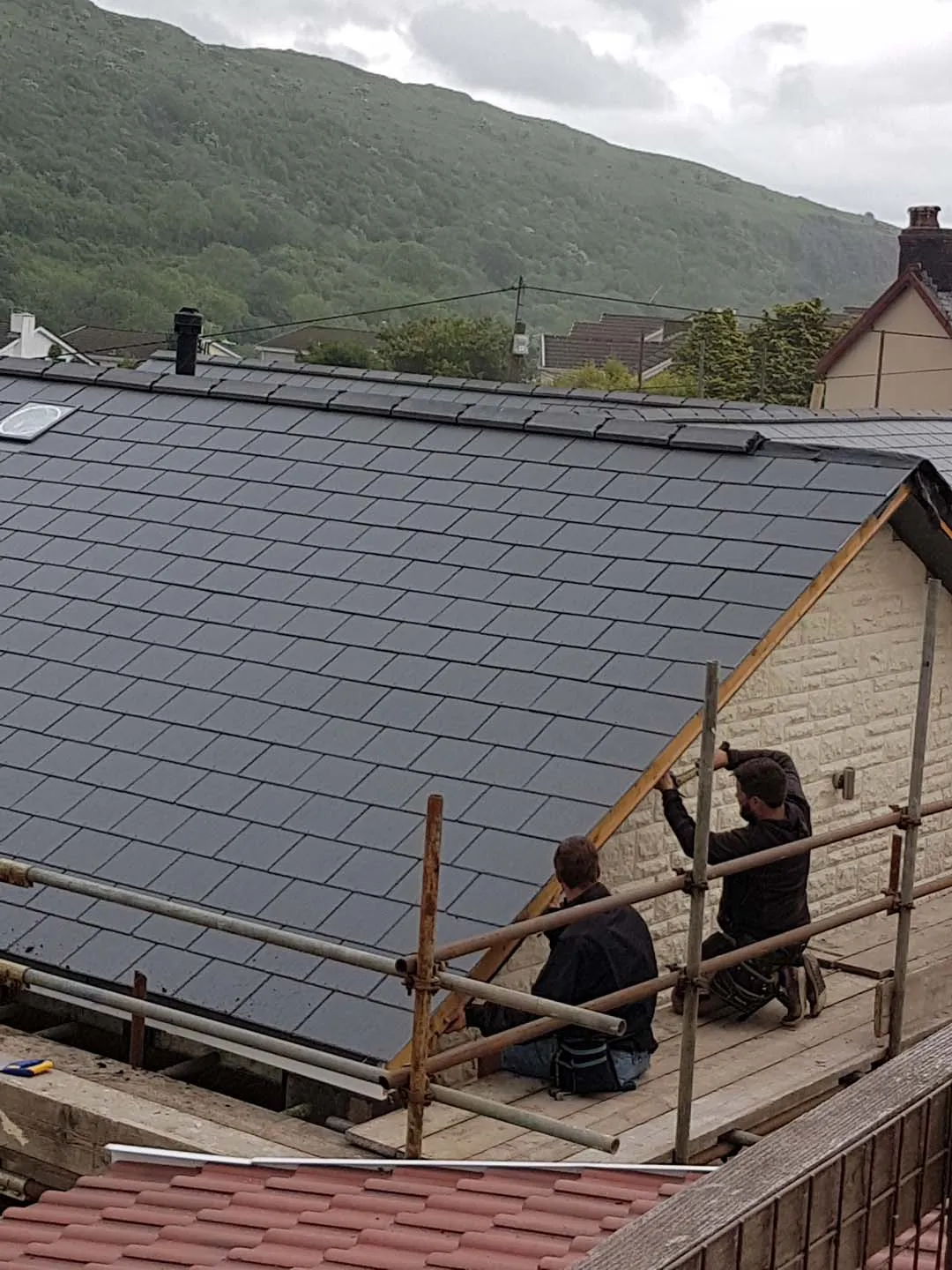 Two roofers on scaffold fixing a timber verge to a newly slated gable