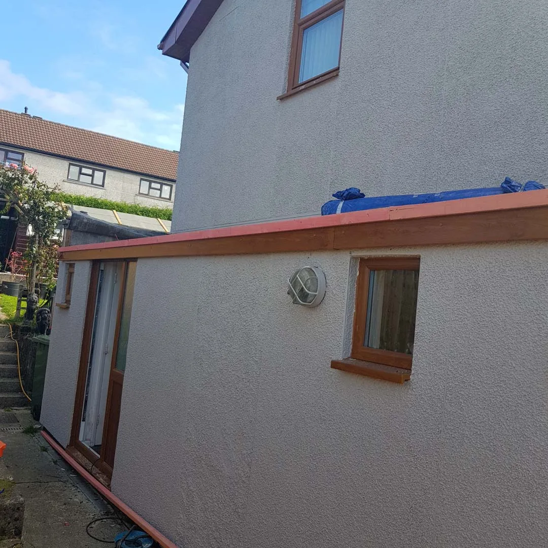 Single-storey building with a new timber fascia and a roll of rubber roofing ready to lay