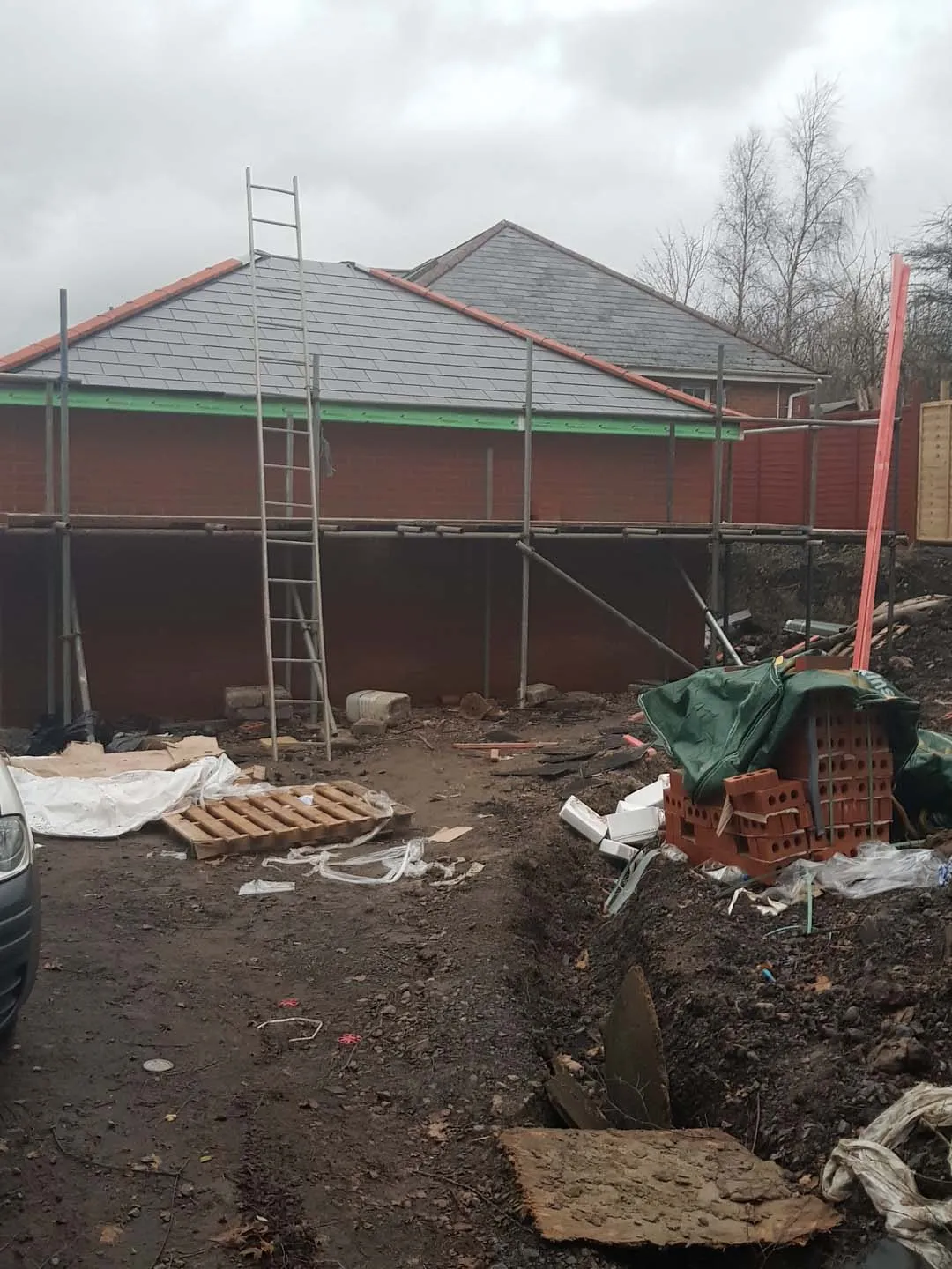 New single-storey building with a hipped slate-effect roof and red hip tiles, scaffold still up
