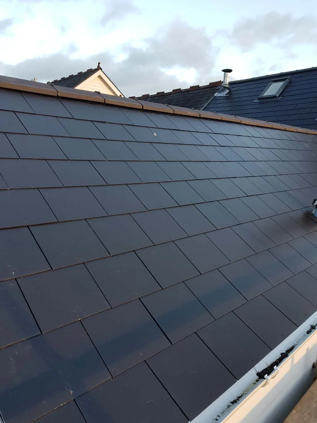 Finished slate-effect tiled roof with a clay ridge and white gutter