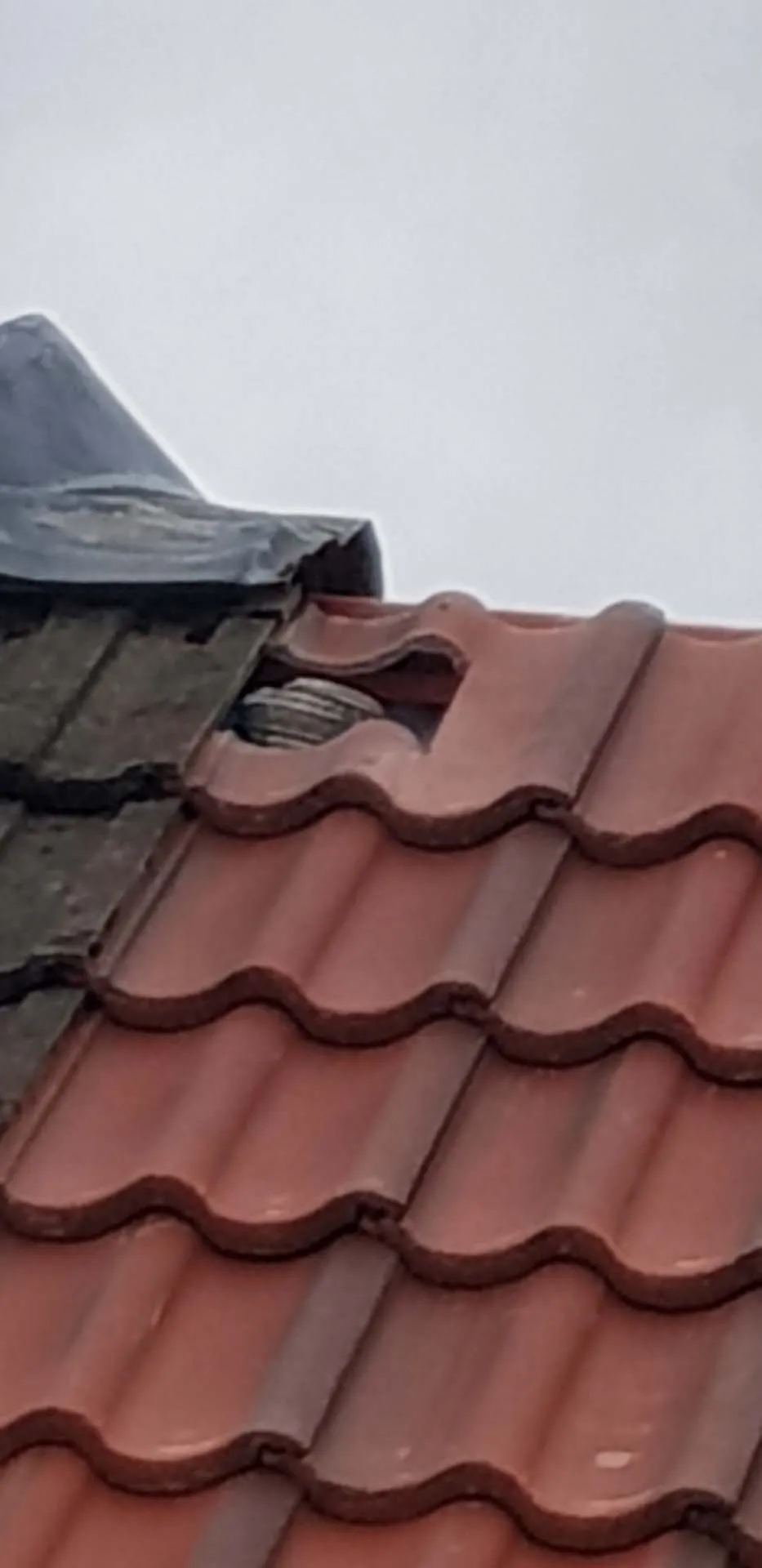 Close-up of a broken roof tile beside the ridge after storm damage